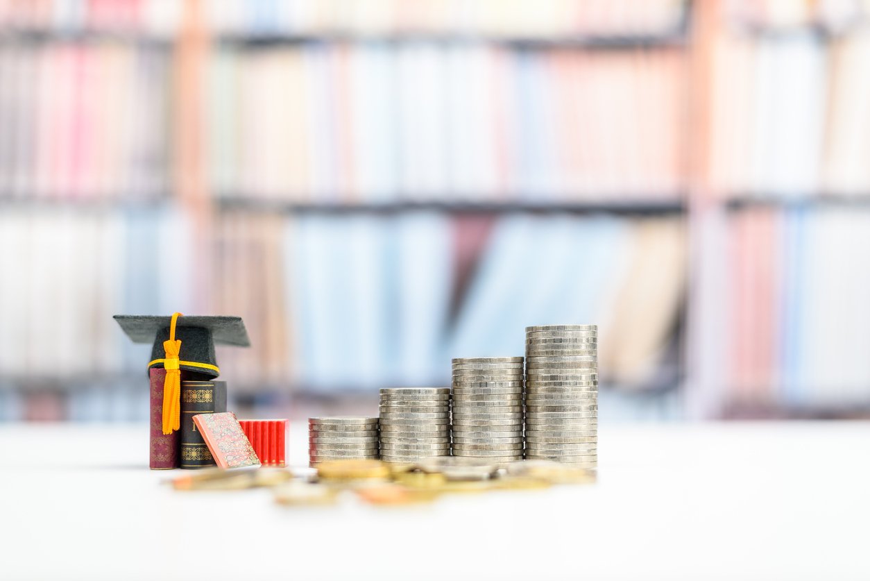 Immagine di copertina dell'articolo sull'educazione finanziaria a scuola con delle monete impilate su un banco di scuola