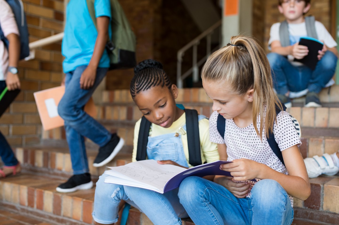 Due alunne consultano insieme un quaderno sui gradini della scuola durante un’attività di apprendimento collaborativo