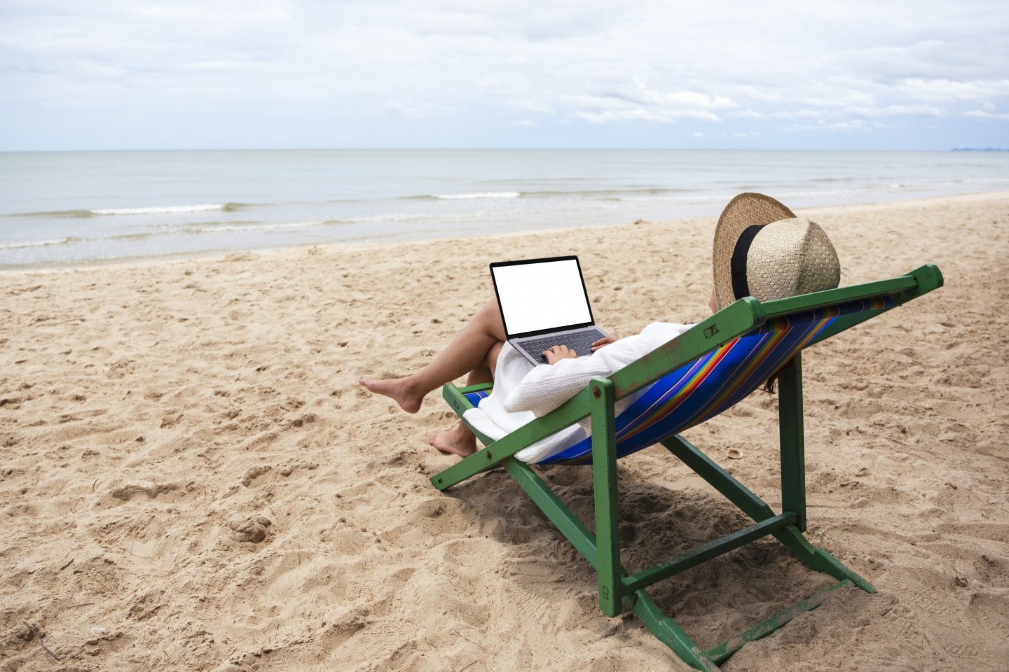 Persona seduta su una sdraio in spiaggia utilizza un computer portatile durante la pausa estiva