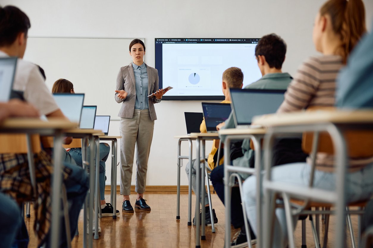 Docente presenta contenuti digitali a una classe di studenti con computer portatili