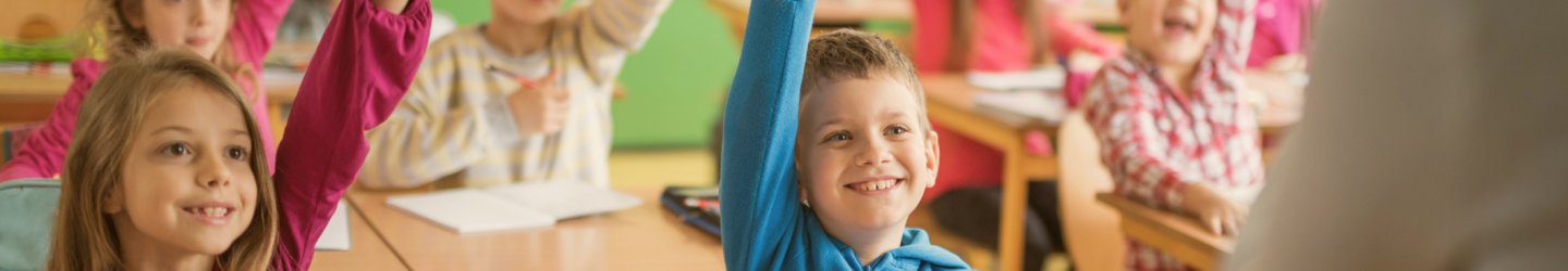 Bambine e bambini in classe con la mano alzata durante un’attività didattica