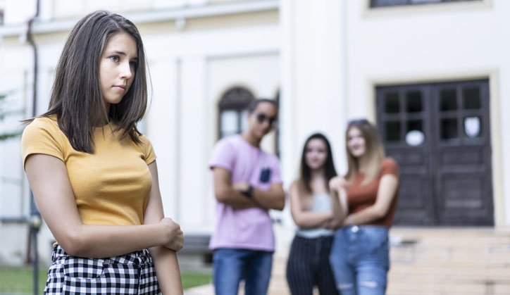 Studentessa davanti alla scuola mentre un gruppo di compagni conversa sullo sfondo